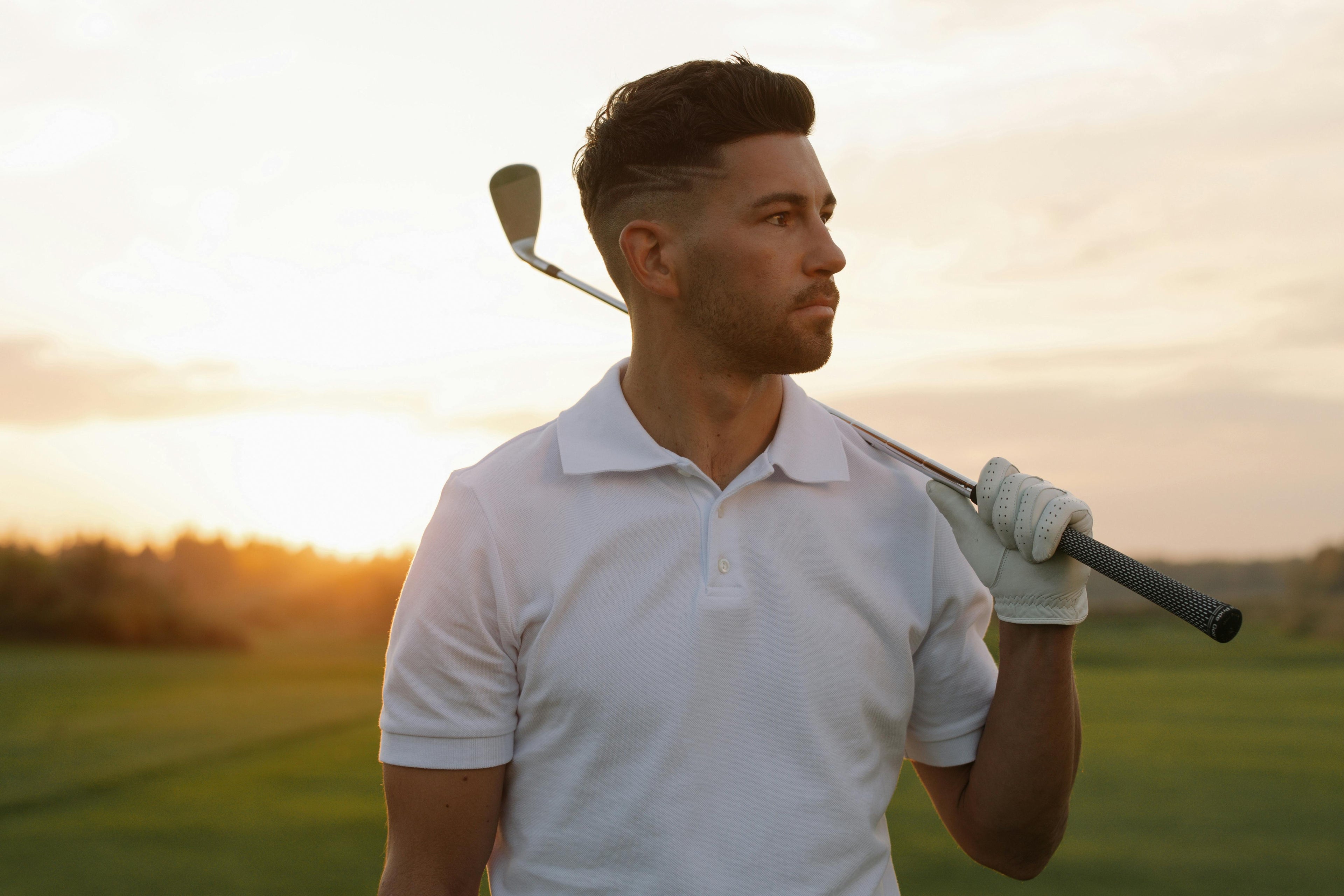 Man holding a golf club on a golf course with a sunset in the background